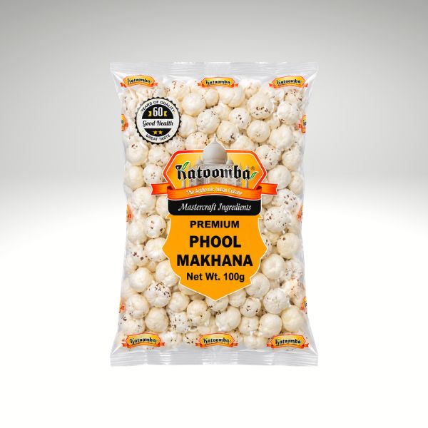 A 100g clear plastic bag of katoomba Premium Phool Makhana on a light gray gradient background. The bag features a prominent yellow and orange label with the katoomba brand logo.