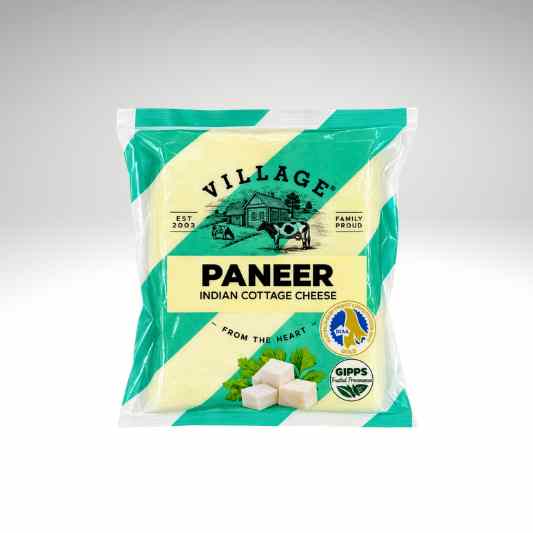 A package of Village Paneer Indian Cottage Cheese, featuring a cream-colored cheese block visible through a clear window in the center of the packaging, surrounded by teal and cream diagonal stripes.