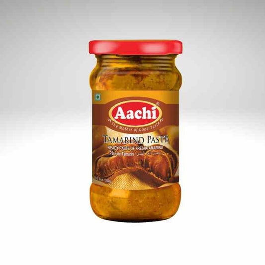 A glass jar of Aachi Tamabind Paste, featuring a red lid and a brown label with the brand logo, set against a light gray gradient background.
