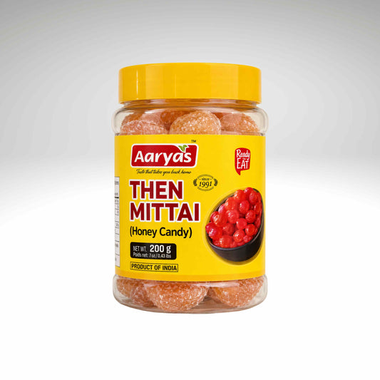 A jar of Aarya's Then Mittai (Honey Candy) with a bright yellow lid and yellow label, containing orange-brown sugar-coated sweets, shown on a light gray gradient background.