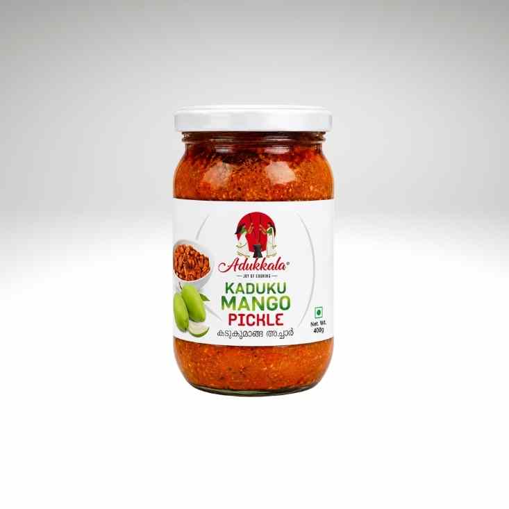 A glass jar of Adukala Kaduku Mango Pickle with a white lid and white label, containing a vibrant red pickle, set against a light gray gradient background.