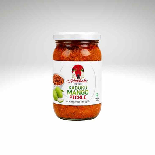A glass jar of Adukala Kaduku Mango Pickle with a white lid and white label, containing a vibrant red pickle, set against a light gray gradient background.