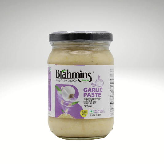 A jar of Brahmins Garlic Paste with a smooth, creamy texture, surrounded by whole garlic cloves and a sprig of fresh herbs, highlighting its rich flavour and versatility in cooking.