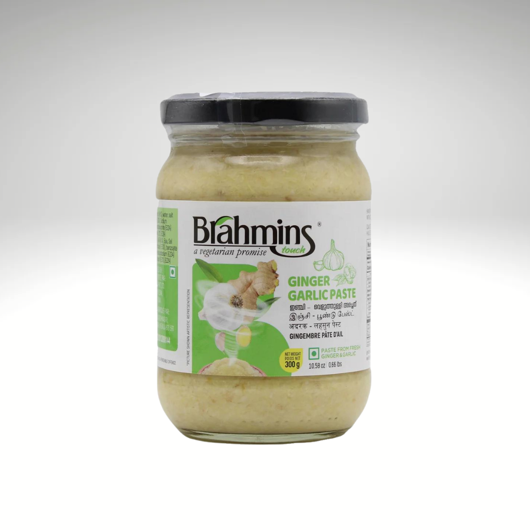 A jar of Brahmins Ginger Garlic Paste, with a creamy texture and a golden hue, placed beside fresh ginger and garlic cloves, emphasizing its fresh ingredients and vibrant flavour.