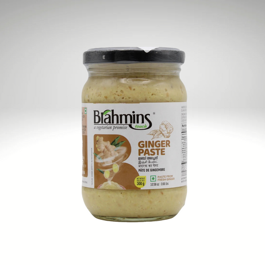 A jar of Brahmins Ginger Paste, showcasing a smooth, golden texture, surrounded by fresh ginger roots and green herbs, emphasizing its aromatic and zesty flavour profile.