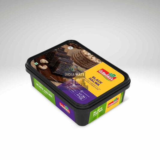 A container of Grandma's Black Halwa, a sweet snack, shown on a light gray gradient background. The packaging features a black plastic tub with a clear lid displaying the dark cake pieces, and colourful side labels in green, purple, and yellow.
